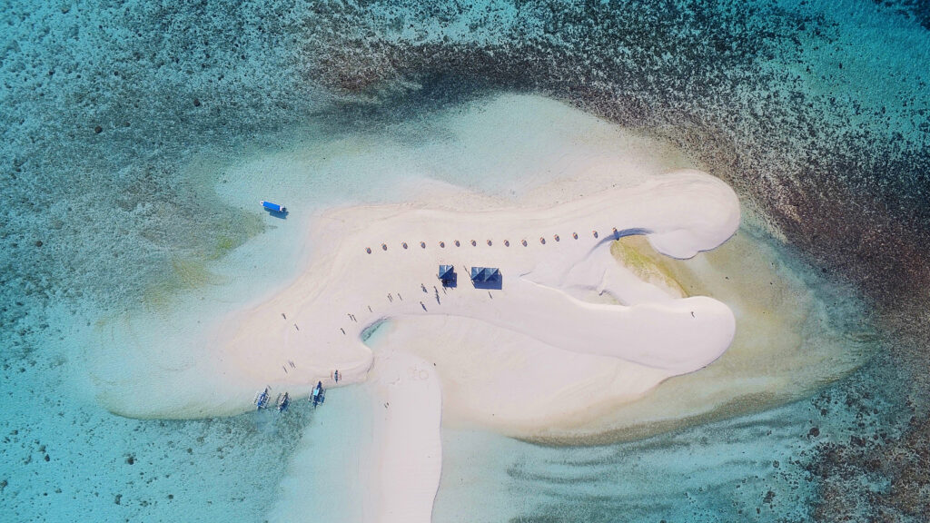 Aerial view of White Island in Camiguin, Philippines—an uninhabited, crescent-shaped sandbar surrounded by clear turquoise waters, with boats and beach huts on the brilliant white sand.