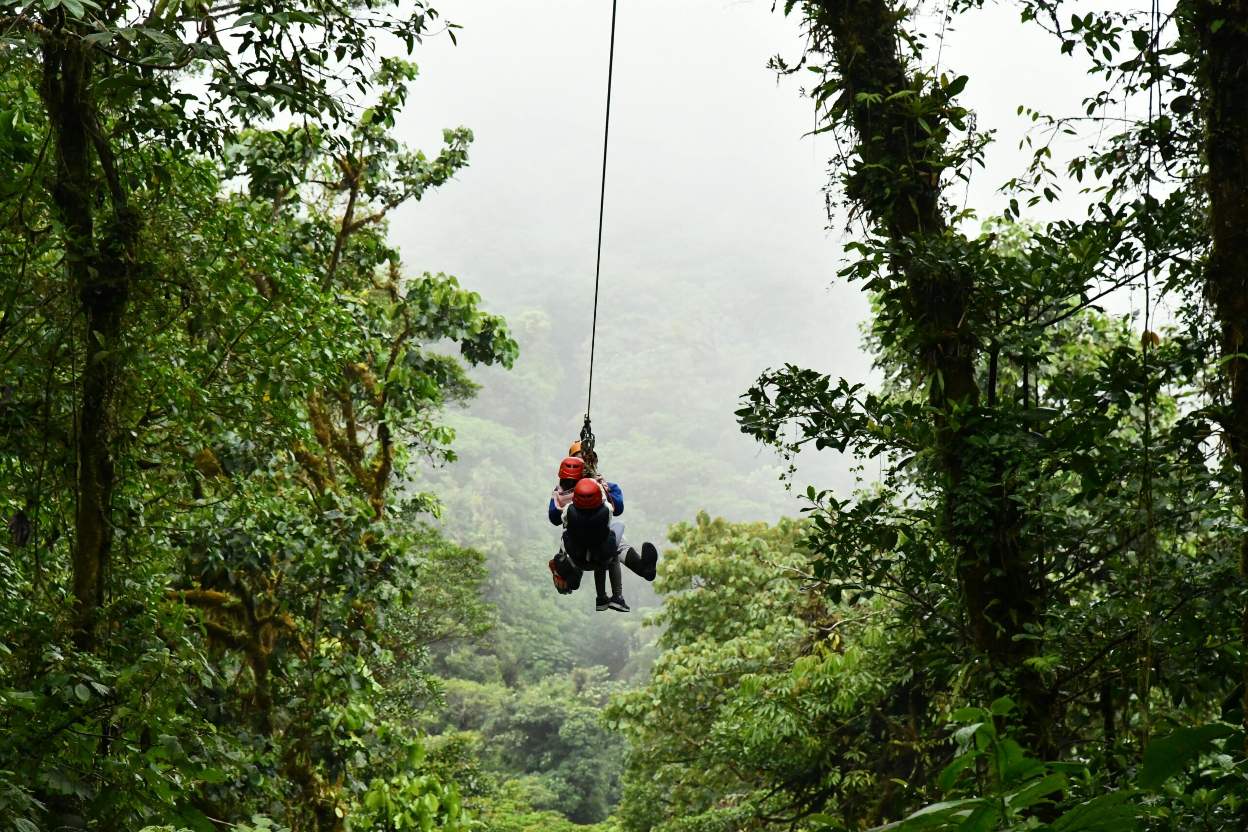 Two people ziplining through a misty rainforest canopy in Costa Rica surrounded by lush green foliage