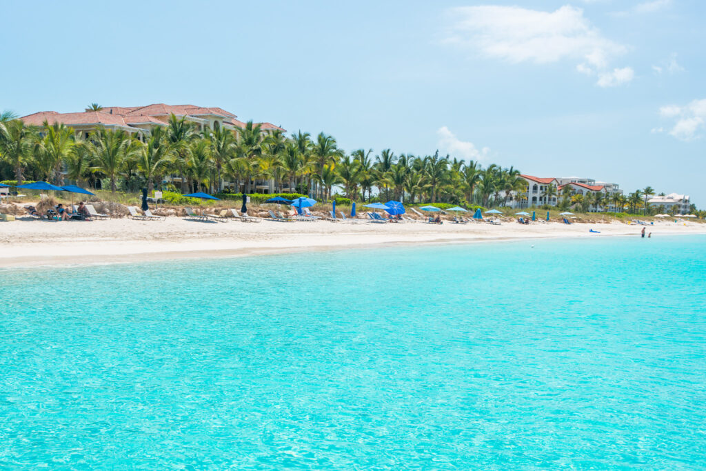 Grace Bay Beach on Providenciales Island, Turks and Caicos, featuring turquoise waters, white sand shoreline, beachfront resorts, and blue beach umbrellas under a sunny sky.