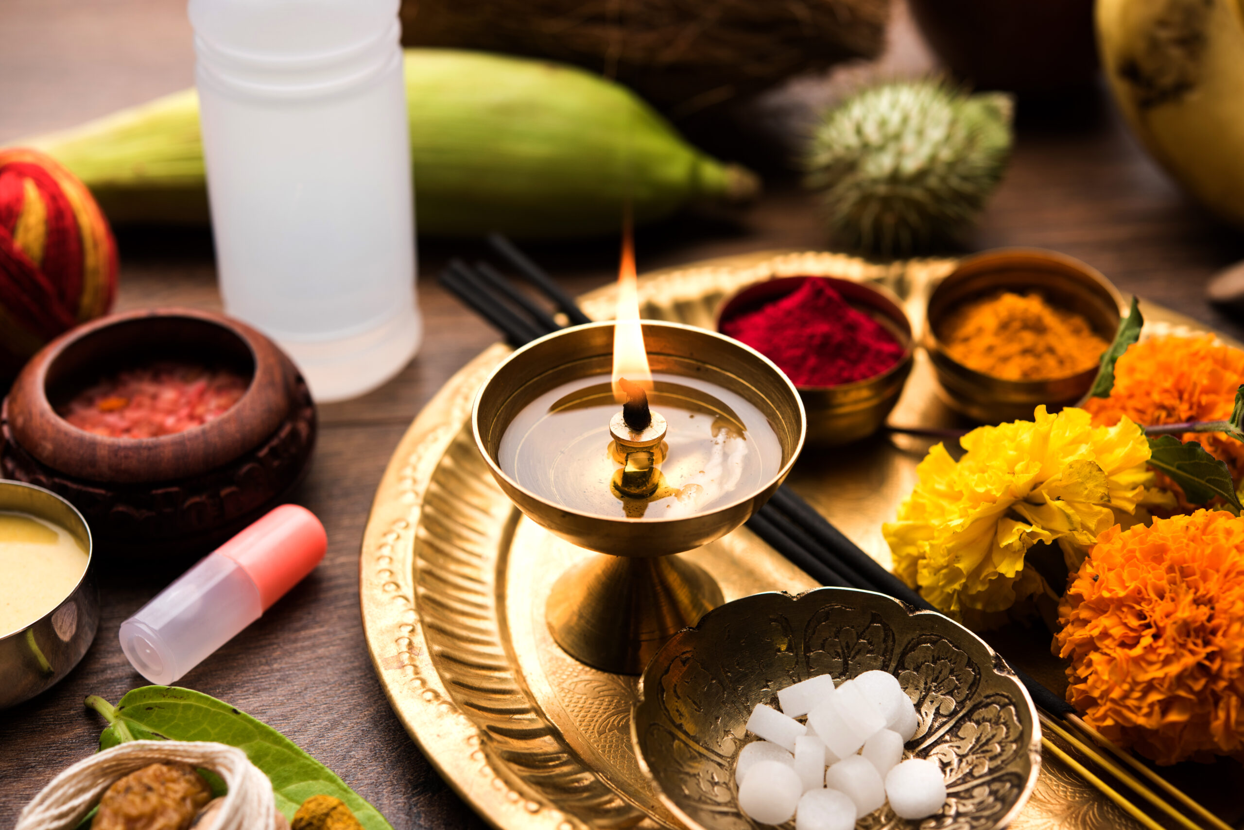 Brass oil lamp, incense sticks, turmeric, kumkum, sugar crystals, marigold flowers, and other sacred items arranged on a golden pooja thali for Hindu worship