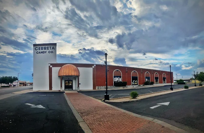 Exterior of Cerreta Candy Company in Glendale, Arizona, featuring its iconic white and brick facade with copper dome entry under a dramatic sky.