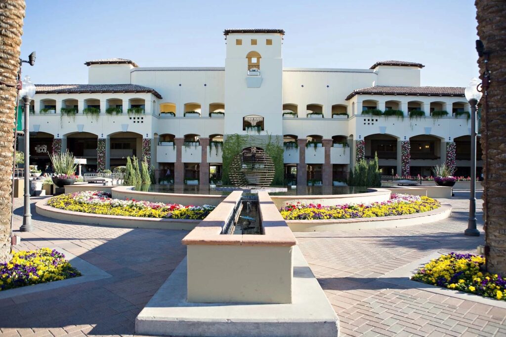 Beautifully landscaped courtyard at the Fairmont Scottsdale Princess in Arizona, featuring colorful flowers, palm trees, a fountain, and resort balconies.