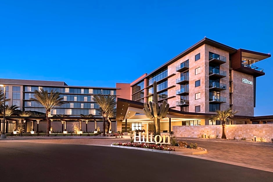 Evening view of Hilton North Scottsdale at Cavasson, Arizona, showcasing the modern architecture, glass balconies, desert landscaping, and illuminated entrance.