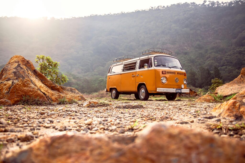 Vintage orange camper van parked in a rugged mountain landscape at sunset — symbolizing road trip freedom, vanlife, and spontaneous travel exploration.