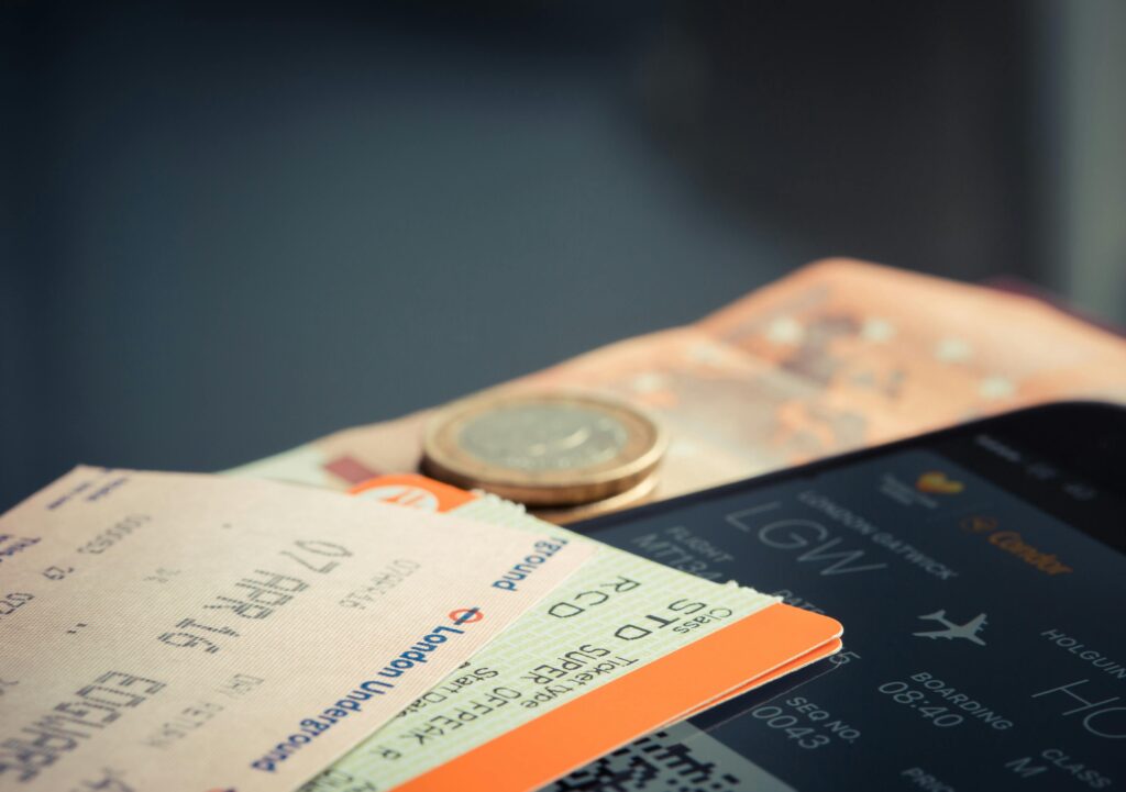 Close-up of a flight boarding pass, train tickets, euro coins, and a smartphone showing a travel itinerary — symbolizing the excitement of booking a trip.