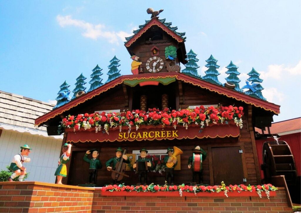 Decorative wooden cuckoo clock with animated figurines, red flowers, and alpine trees at Sugarcreek, Ohio Swiss Village