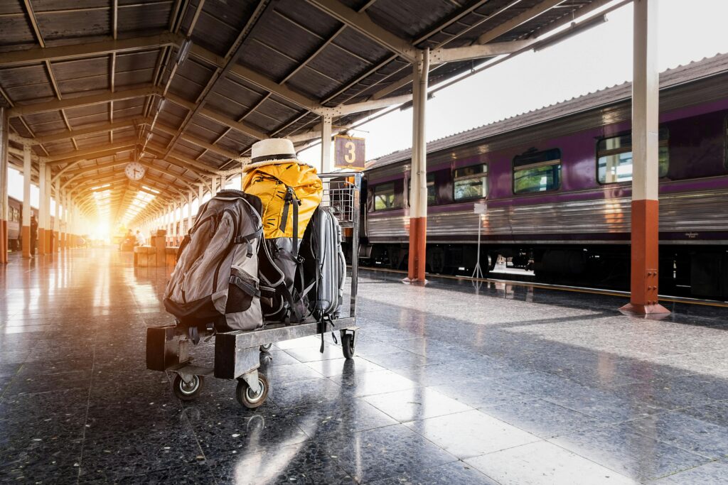 Backpacks and travel gear on a trolley at a train station platform, with a hat atop a yellow bag — symbolizing smart packing and light travel essentials.