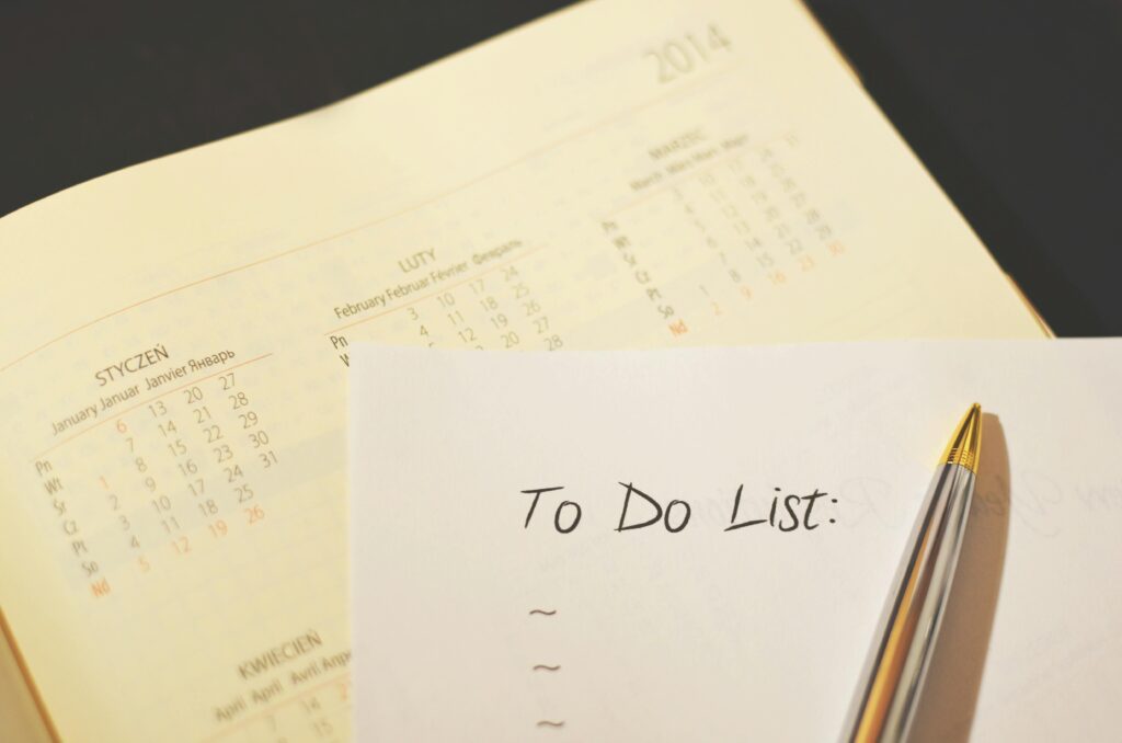 Close-up of a handwritten to-do list with a pen resting on paper, placed over a calendar — representing task planning, productivity, and adult responsibilities.