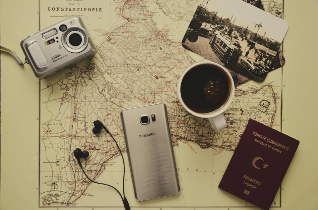 Flat lay of vintage travel items on a historic map of Constantinople, including a Turkish passport, retro Kodak camera, Samsung phone, coffee, old photo, and earphones.