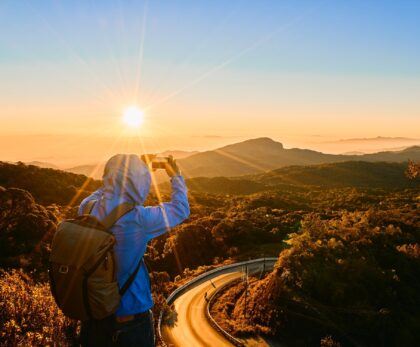 Backpacker taking a photo of a sunrise over a mountain landscape — symbolizing hidden gem travel moments – Travel Crock