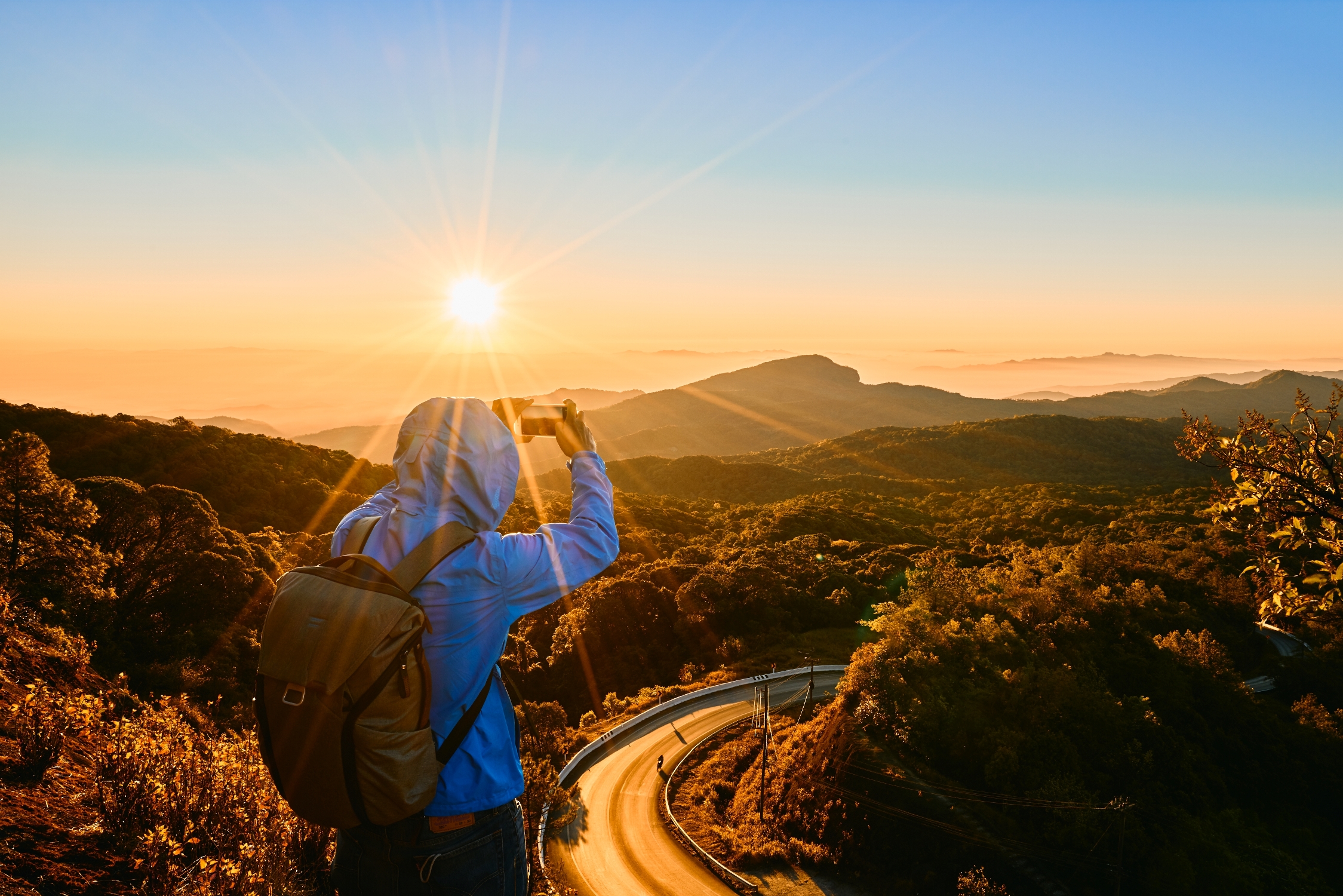 Backpacker taking a photo of a sunrise over a mountain landscape — symbolizing hidden gem travel moments – Travel Crock