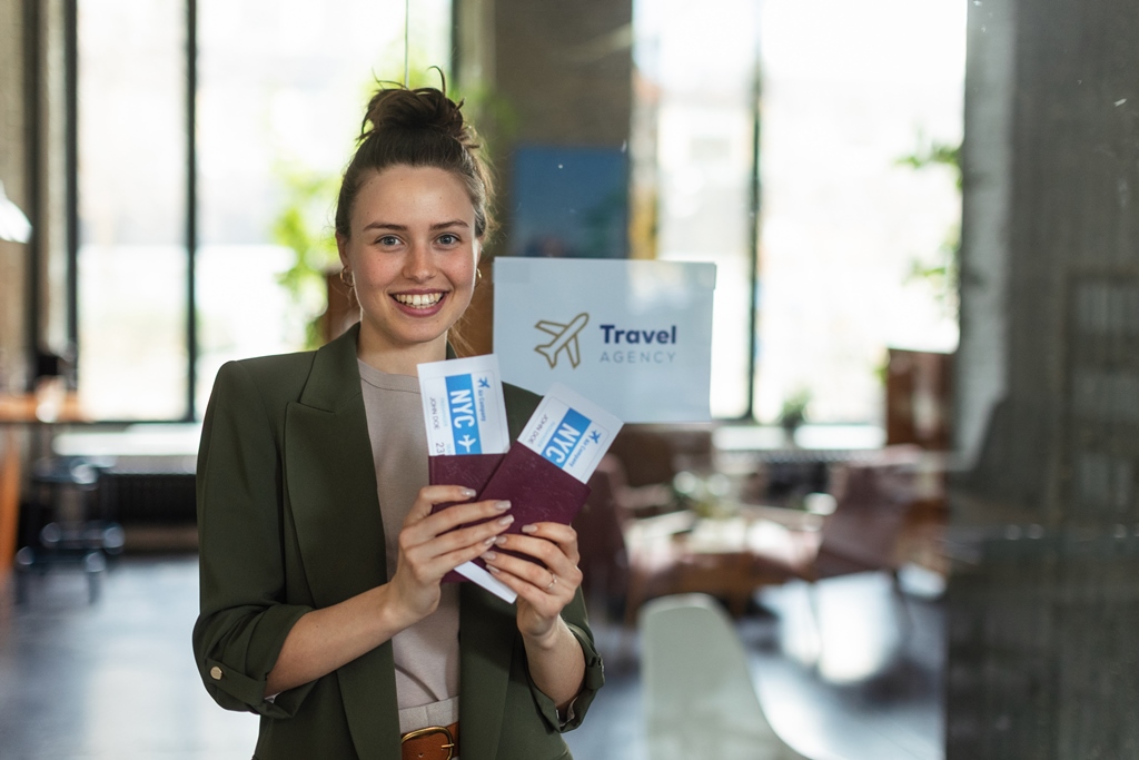 Smiling woman holding NYC plane tickets and a passport at a modern travel agency, showcasing easy and joyful booking with Travel Crock.
