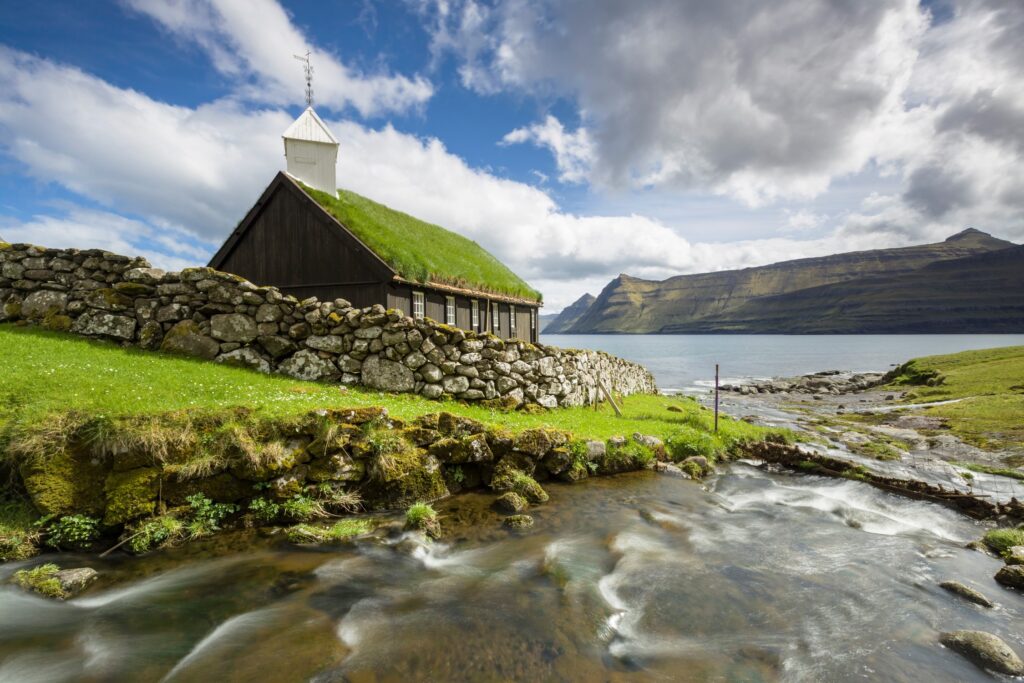 Scenic view of a grass-roof church and stone wall by the sea in Funningur, Faroe Islands, Denmark – Travel Crock