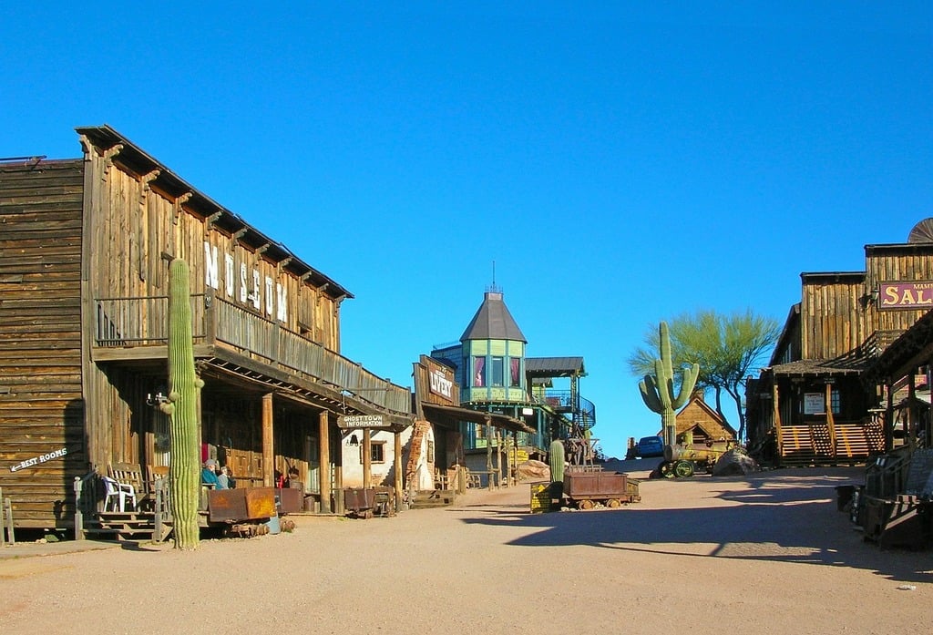 Historic wooden buildings and Old West architecture in Goldfield Ghost Town, Arizona, with desert cacti and clear blue skies.
