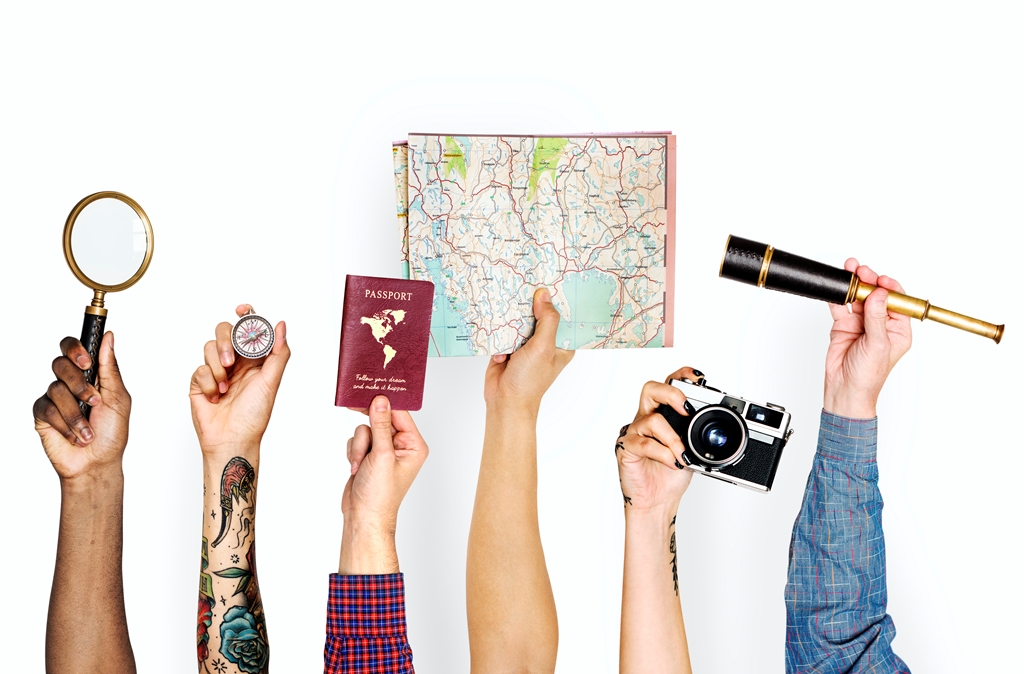 Diverse hands holding travel items including a magnifying glass, compass, passport, map, vintage camera, and telescope—Travel Crock adventure concept