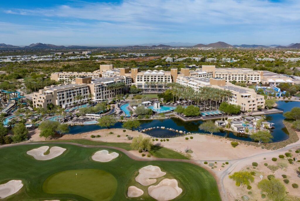 Aerial view of JW Marriott Phoenix Desert Ridge Resort in Arizona, showcasing palm trees, golf course, lazy river, pools, and scenic mountain backdrop.