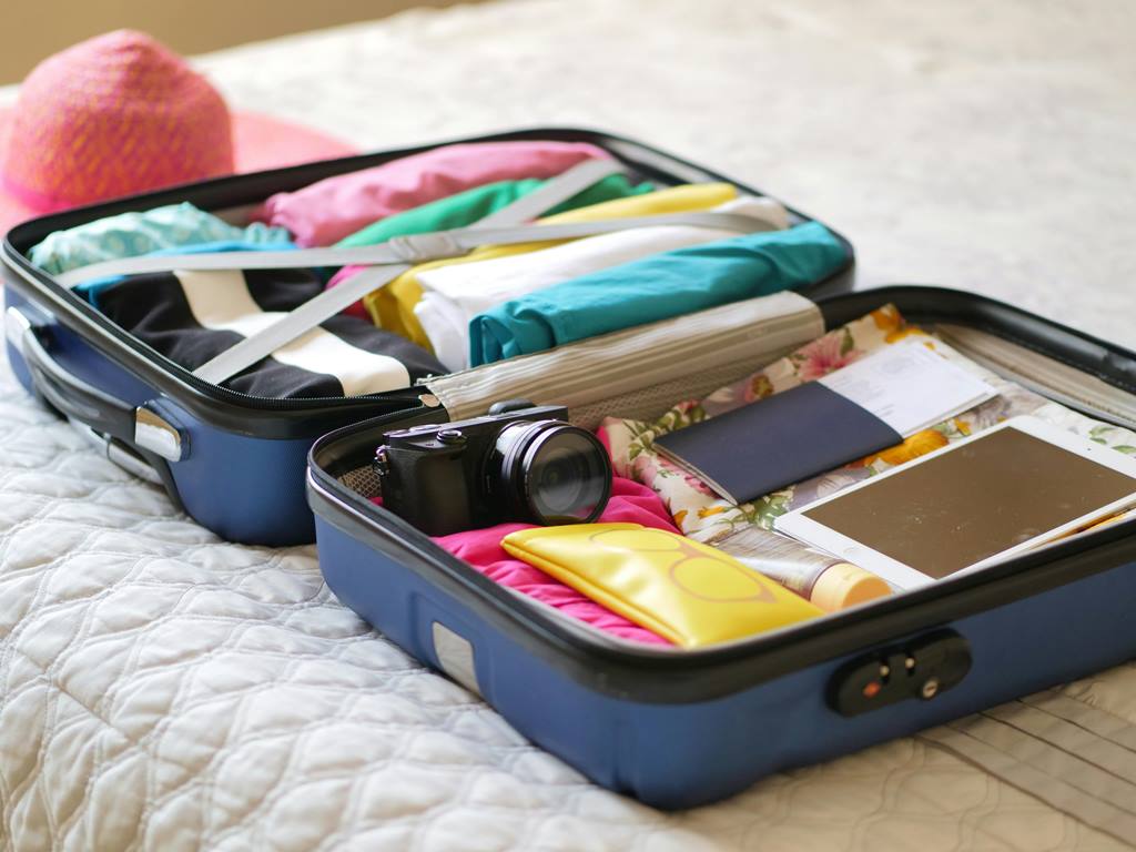 Open suitcase packed with clothes, camera, passport, tablet, and travel essentials—ideal for adding smart luggage trackers with Travel Crock