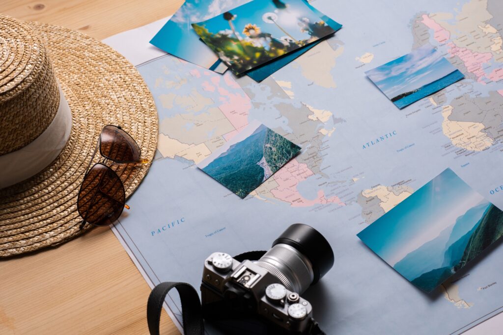Flat lay of travel essentials including a map, straw hat, sunglasses, vintage camera, and travel photos – Travel Crock