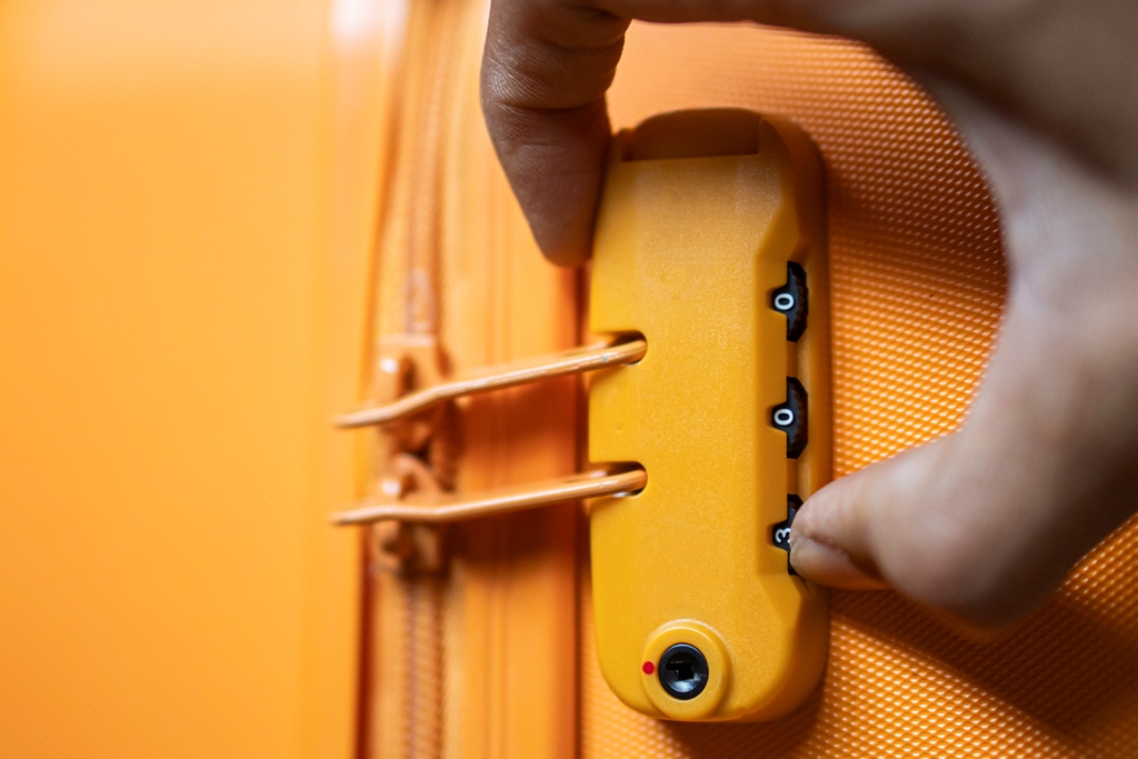 Close-up of a hand setting a combination lock on a bright yellow suitcase—essential travel safety tip from Travel Crock