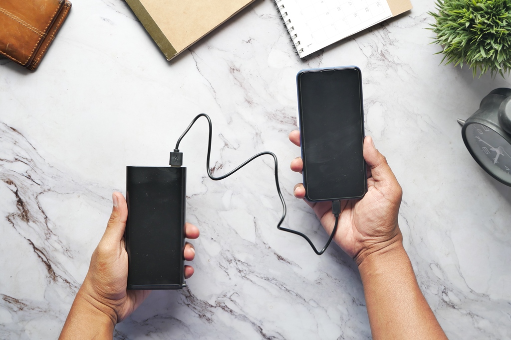 Hands holding a smartphone and a power bank connected with a cable—must-have portable charging gear for travelers with Travel Crock