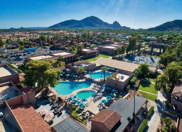 Aerial view of The Scottsdale Plaza Resort & Villas in Arizona, featuring pools, palm trees, terracotta-roofed villas, and Camelback Mountain in the background.