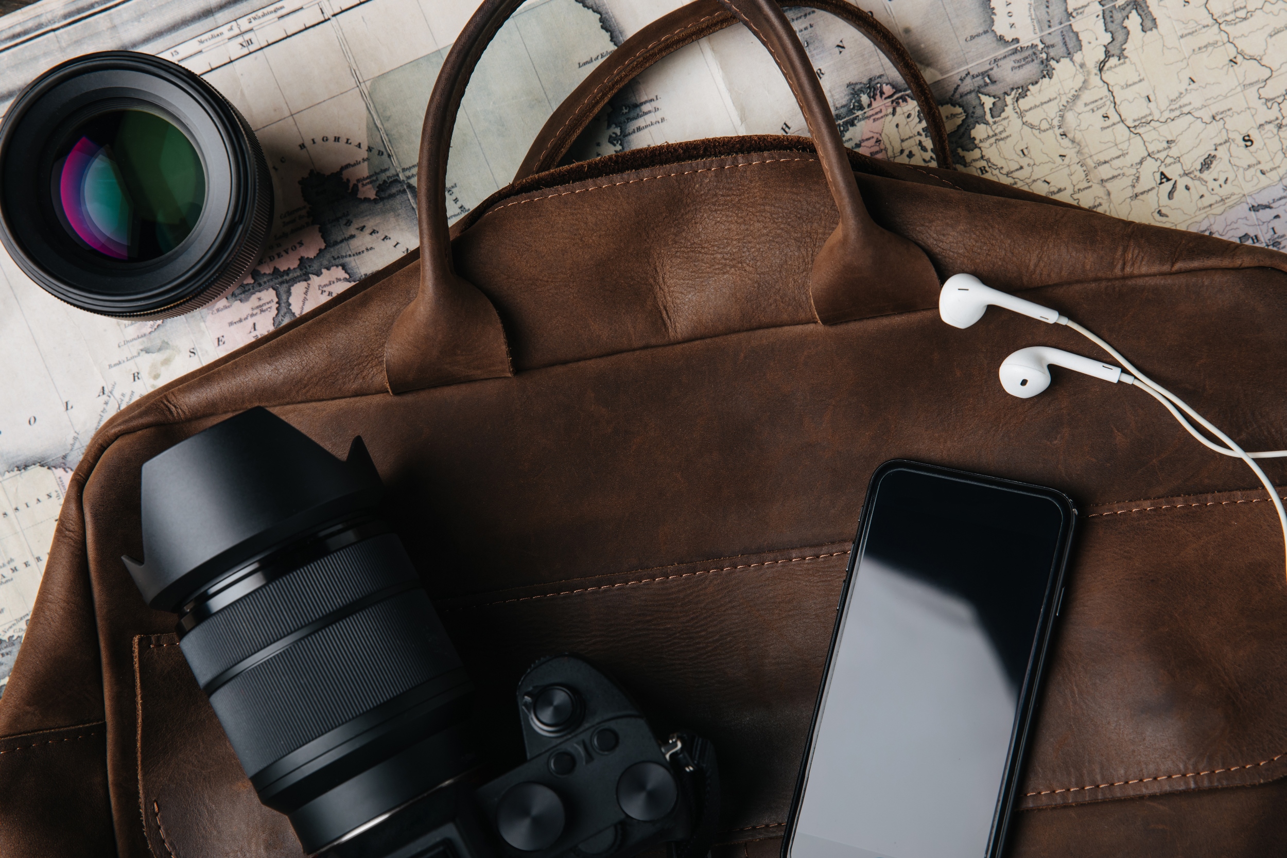 Flat lay of travel essentials including leather bag, camera, smartphone, earbuds, and lens on vintage world map — perfect for Travel Crock adventures