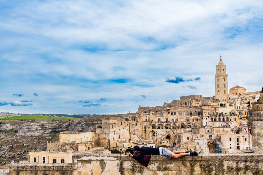 Tourist resting on a stone ledge overlooking the ancient cave city of Matera, Italy – Travel Crock
