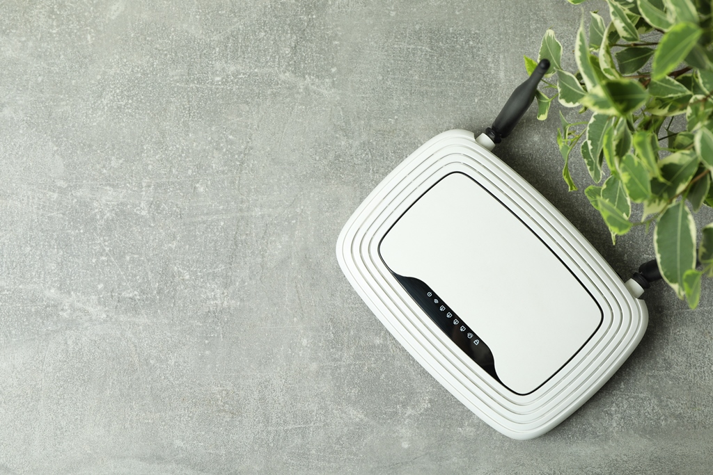 Flat lay of a white mobile Wi-Fi router on a gray surface next to green leaves—ideal for staying connected while traveling with Travel Crock