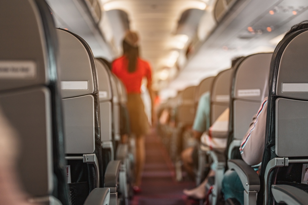 Flight attendant walking down airplane aisle during a long-haul flight, viewed from a passenger seat – perfect visual for comfort travel tips by Travel Crock.
