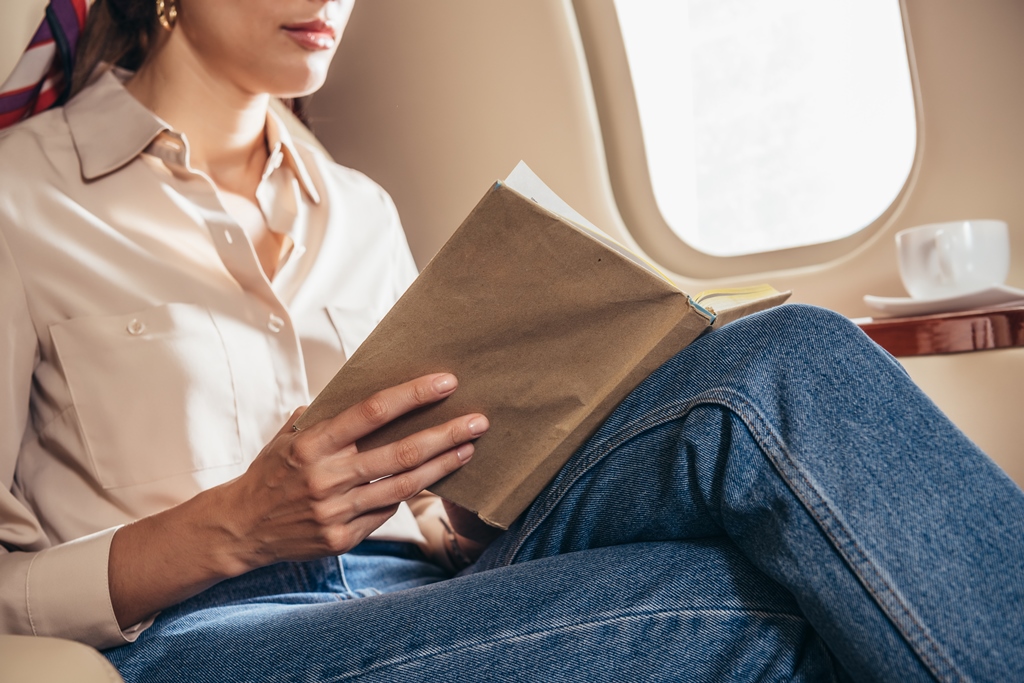 Woman reading a book on an airplane near the window—peaceful inflight moment recommended by Travel Crock for long travel comfort.
