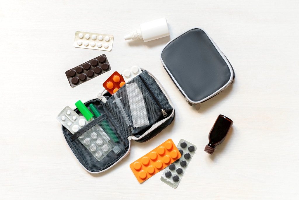 Flat lay of a travel health pouch with blister packs, medicine bottles, syringes, and nasal spray—smart carry-on essentials by Travel Crock.