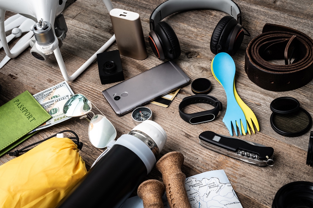 Flat lay of travel essentials on wooden background—passport, power bank, headphones, gadgets, cash, and personal accessories for long flights by Travel Crock.